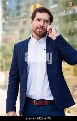 Successful young businessman in a suit having a conversation on his cellphone while walking alone through the city Stock Photo
