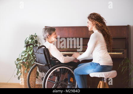 A girl with grandmother in wheelchair by the piano. Stock Photo