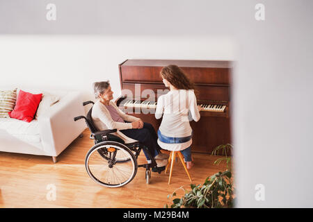 A girl with grandmother in wheelchair playing the piano. Stock Photo