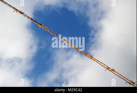 Rusty barbed wire against a blue sky with white clouds Stock Photo
