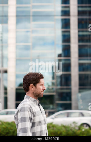 Profile of a casually dressed young man standing by himself in front of buildings on a city street Stock Photo