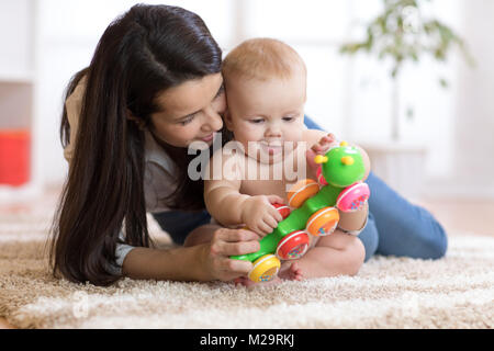 Mother and her baby son play with toy in cosy children room Stock Photo