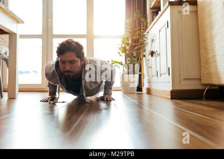 Fit young man in sportswear straining while doing pushups on the floor of his apartment during a workout Stock Photo