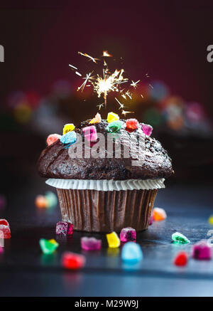 Delicious and funny Chocolate Muffin with candies and sparkler on wooden table. Bokeh background. Selective focus. Copy space. Stock Photo