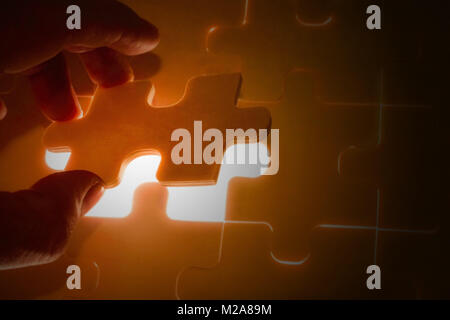 Hand holding a missing jigsaw puzzle piece with light glow, business concept for completing the final puzzle piece Stock Photo