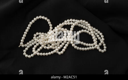 A string of old fake pearls on a black fabric background.