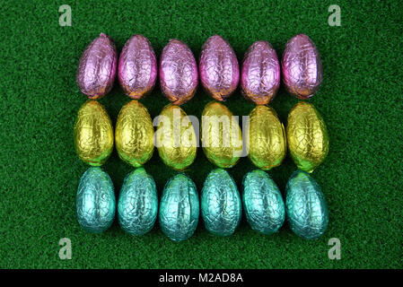 Easter time chocolate eggs wrapped in shiny foil and laid in a line on grass Stock Photo