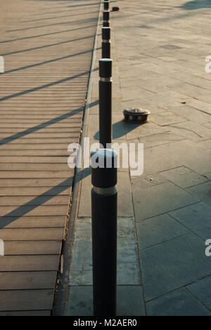 A line of bollards casting long shadows across a boardwalk in Barcelona, Spain Stock Photo