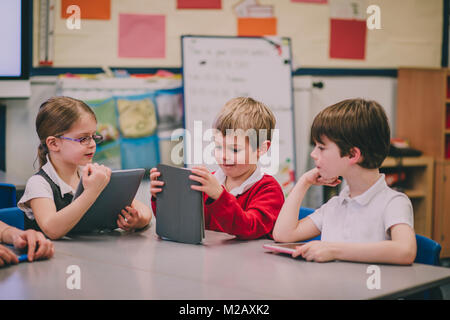 Table of primary school students in a classroom are using digital tablets to work on. Stock Photo