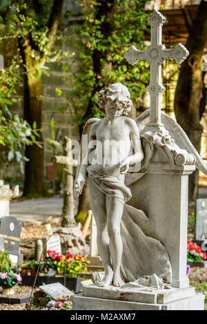 stone sculpture of boy angel  at historical monumental Staglieno Cemetery in town, shot in bright  winter light  in Genova, Liguria, Italy Stock Photo