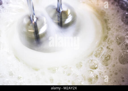 Mixer in motion whipping frothy egg whites in a bowl to make meringue Stock Photo