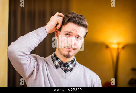 Confused or doubtful young man scratching his head and looking up Stock Photo