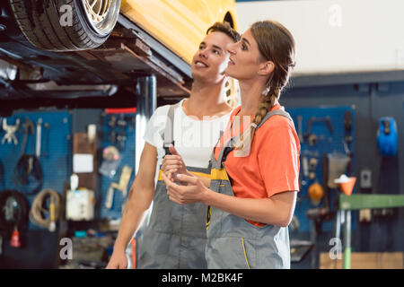 Two dedicated auto mechanics smiling happy, while checking the modified wheels of a tuned car after working together in a modern automobile repair sho Stock Photo