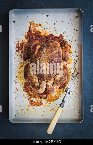 Roast chicken with a herbal crumb on a roasting tray on a slate background. UK