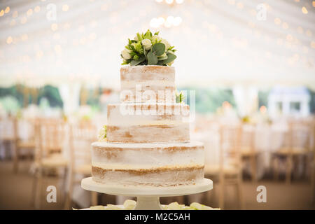 Three tiered wedding cake topped with flowers, in empty marquee Stock Photo
