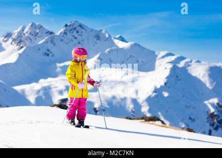 Child skiing in mountains. Active toddler kid with safety helmet, goggles and poles. Ski race for young children. Winter sport for family. Kids ski le Stock Photo