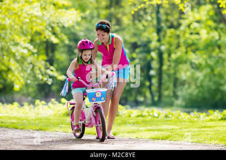 Child riding bike. Kid on bicycle in sunny park. Mother teaching little girl to cycle. Preschooler learning to balance wearing safe helmet. Sport for  Stock Photo