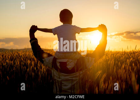Father carrying son on shoulders in field of wheat at sunset Stock Photo