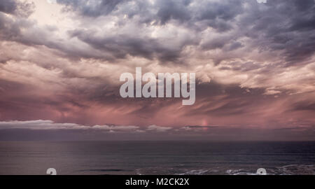 Stormy sky and vertical rainbow over the sea at sunset. Stock Photo