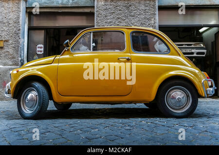 Fiat 500 fabricated in 1970. Old style, classic, vintage, retro car. Yellow color. Parked outside an auto repair shop in Rome, Italy, EU. Side view. Stock Photo