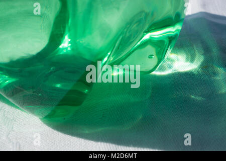 A closeup of sun and shadows cast through the bottom of a green plastic bottle with a petaloid base. Stock Photo