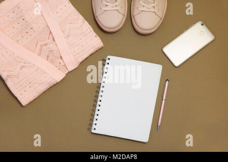 flat lay with a blank note book, phone and pen in coral on a brown background Stock Photo