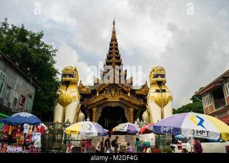 Entrance to Shwedagon pagoda, with pair of yellow Chinthe lion-like statues gurading and protecting pagoda, umbrellas in street market Yangon, Burma Stock Photo