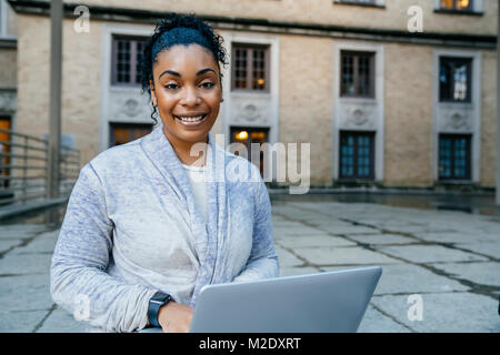 Portrait of smiling Black woman using laptop outdoors Stock Photo