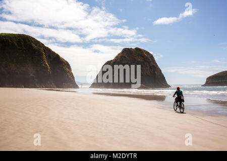 Distant Caucasian woman riding bicycle on beach Stock Photo