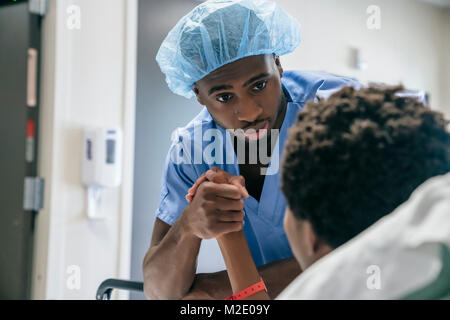 Black doctor holding hand of boy in hospital bed Stock Photo