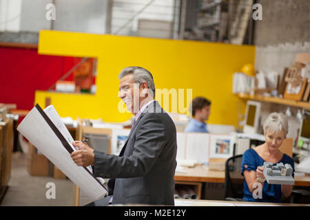 Smiling architect reading blueprint in office Stock Photo