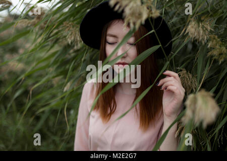 Pensive Asian woman standing in field of tall grass Stock Photo