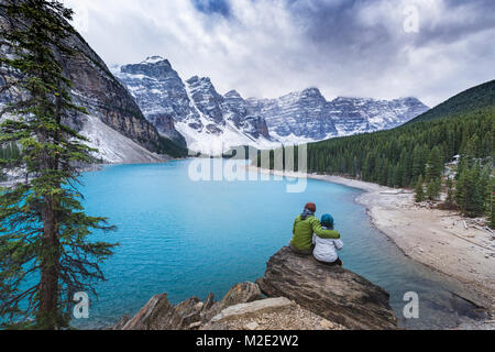 Asian couple sitting on rock admiring scenic view of mountain lake Stock Photo