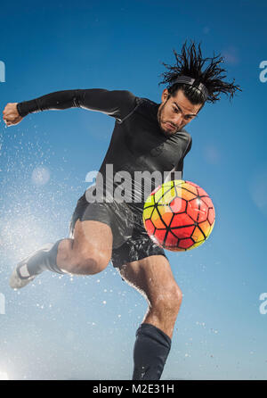 Water splashing on Hispanic man kicking soccer ball Stock Photo