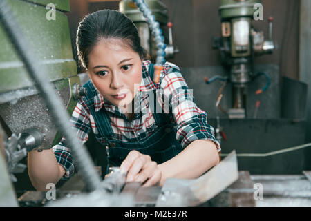 selective focus photo of beautiful young female lathe machine factory worker using company device doing milling parts work. Stock Photo