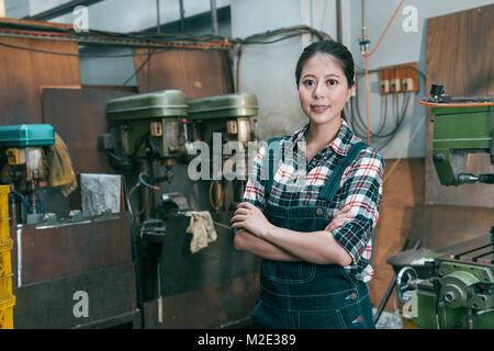 confident happy lathe factory woman employee hands crossed put on chest standing in milling machine department and face to camera smiling. Stock Photo