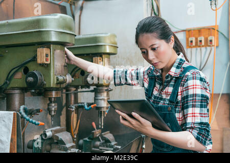 beautiful young lathe company female leader control drilling machine and using mobile digital tablet confirm processing status. Stock Photo