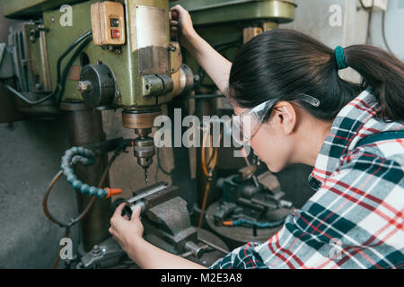 elegant attractive woman worker wearing safety goggles using lathe machine to drill components. Stock Photo