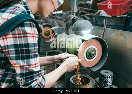 young professional female milling machine company employee wearing safety glasses working on grinding wheel and processing components with sparks in w Stock Photo