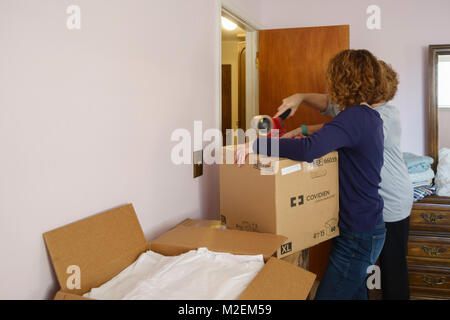 Two Caucasian women work together to tape a moving box shut in preparation to moving out of town. Oklahoma, USA. Stock Photo