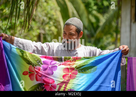 KRABI, THAILAND - MAY 2, 2015: Muslim man drying Batik fabric  outside home in Lanta island of Krabi, Thailand Stock Photo