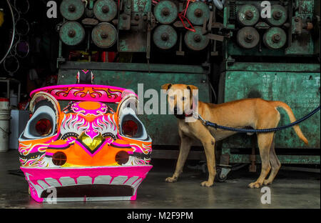 SUBANG, MALAYSIA - FEBRUARY 07: A dog stand near the traditional Chinese Lion head inside the Wan Seng Hang (WSH) Dragon & Lion Arts workshop in Subang outside Kuala Lumpur on February 7, 2018. WSH produce around 500 lion heads per year with some being exported to Asia including Taiwan, Japan, Hong Kong, United States and around the world. The traditional Lion Head certain combinations of colour and design were created as a tribute to famous Chinese historical, entire process is done by hand and rattan is used to form the skeletal structure of the head with layers of bamboo paper. The price of Stock Photo