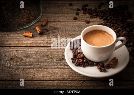 A cup of coffee on old wooden table with some beans and some cinnamon's sticks Stock Photo