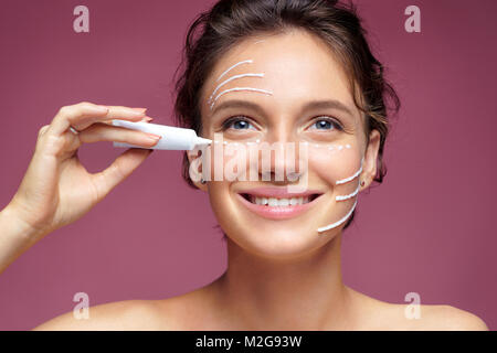 Beautiful smiling woman using cream around the eyes. Photo of woman with perfect skin on pink background. Skin care and beauty Stock Photo