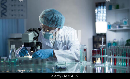 Medical lab worker examining laboratory glass with sample through microscope, stock video Stock Photo