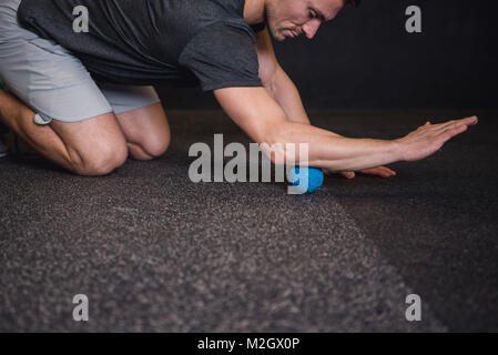 Caucasian man in his 30s stretching and rolling out muscles after workout. Stock Photo