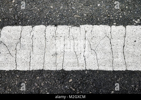Close up picture of an asphalt road with a cracked white lane marking. Stock Photo