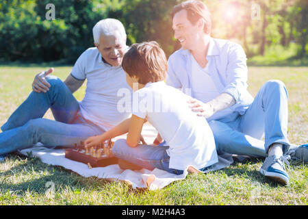 Father and granddad teaching little boy playing chess Stock Photo