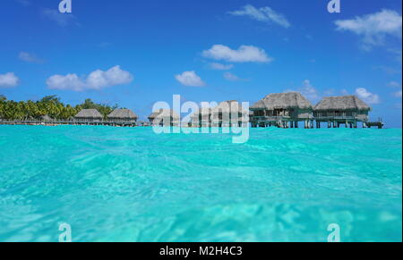 Over water bungalows with thatched roof in a tropical lagoon, seen from sea surface, Tikehau atoll, Tuamotus, French Polynesia, Pacific ocean, Oceania Stock Photo