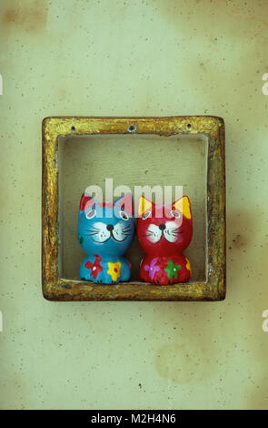Two comical small wooden models of coloured cats with large heads and small bodies in gold framed box Stock Photo